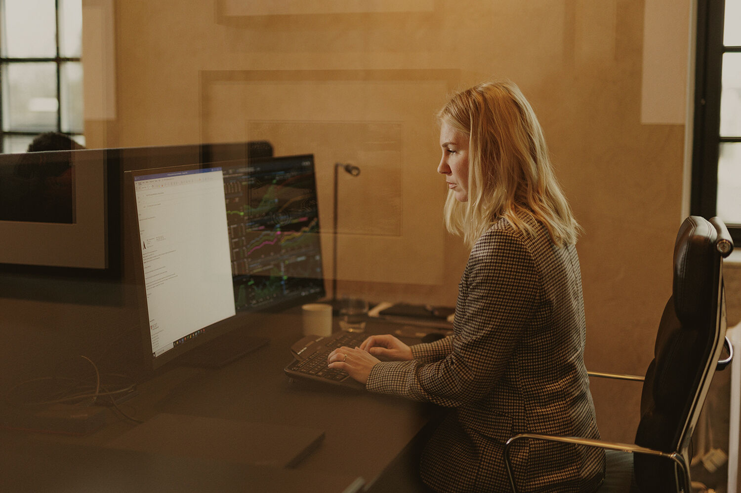 Kvinne ved kontorpult med skjermer som viser grafer, tall og tabeller
