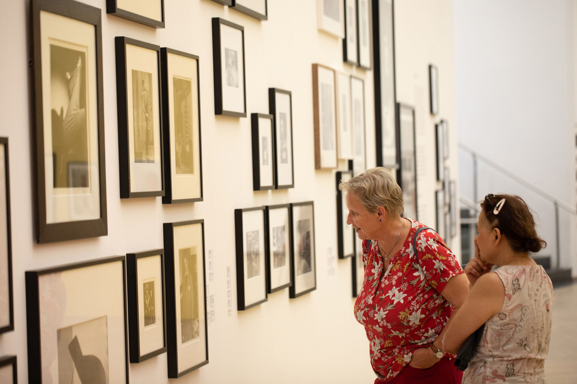 To kvinner studerer mange små innrammede bilder som fyller en gallerivegg