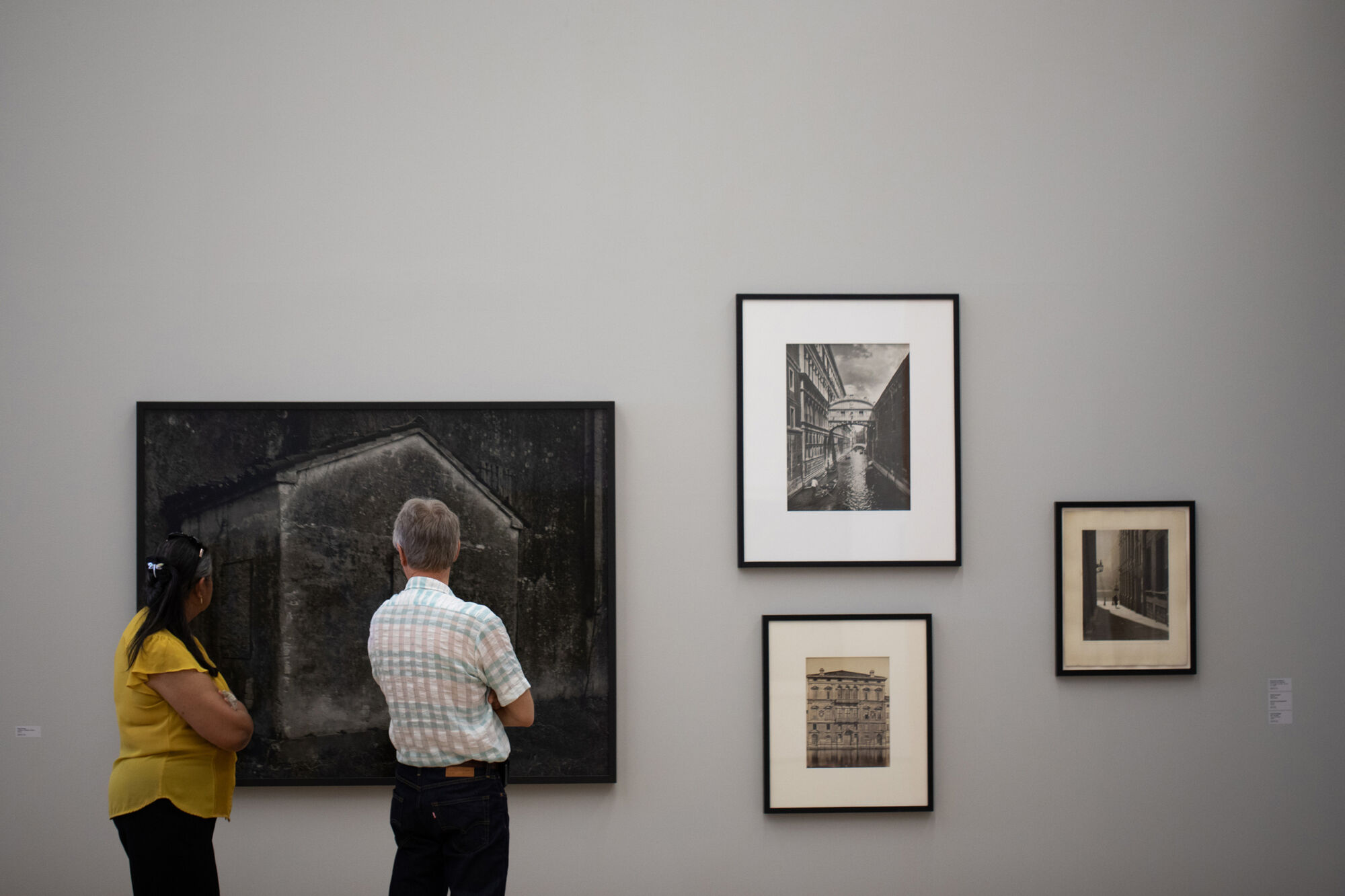 To personer studerer fotografier på en gallerivegg